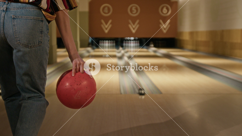 Young adult woman rolling bowling ball down lane, striking pins and cheering at success. Marketing campaigns promoting indoor sports, active lifestyle, or weekend recreational activities
