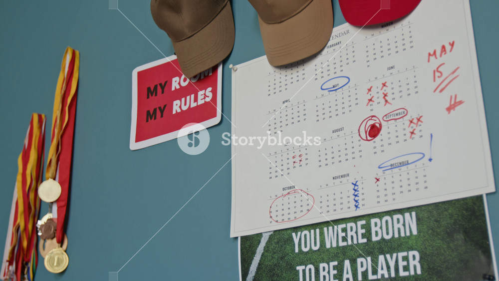 Closeup detail shot of various wall decor in teenagers room with focus on calendar with red markings and lettering You were born to be a player, copy space