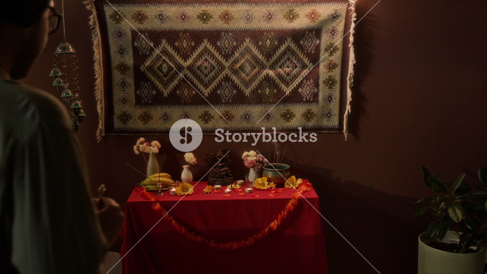 Medium long shot of Indian man in traditional turban and kurta coming to home Hindu altar and decorating it with offerings and bell, checking smouldering incense sticks before praying