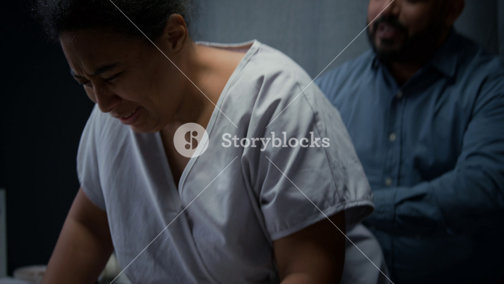 Black pregnant woman leaning on hospital bed rail,breathing through painful labor contractions while husband rubs her back. Footage suits maternity care and childbirth promotions