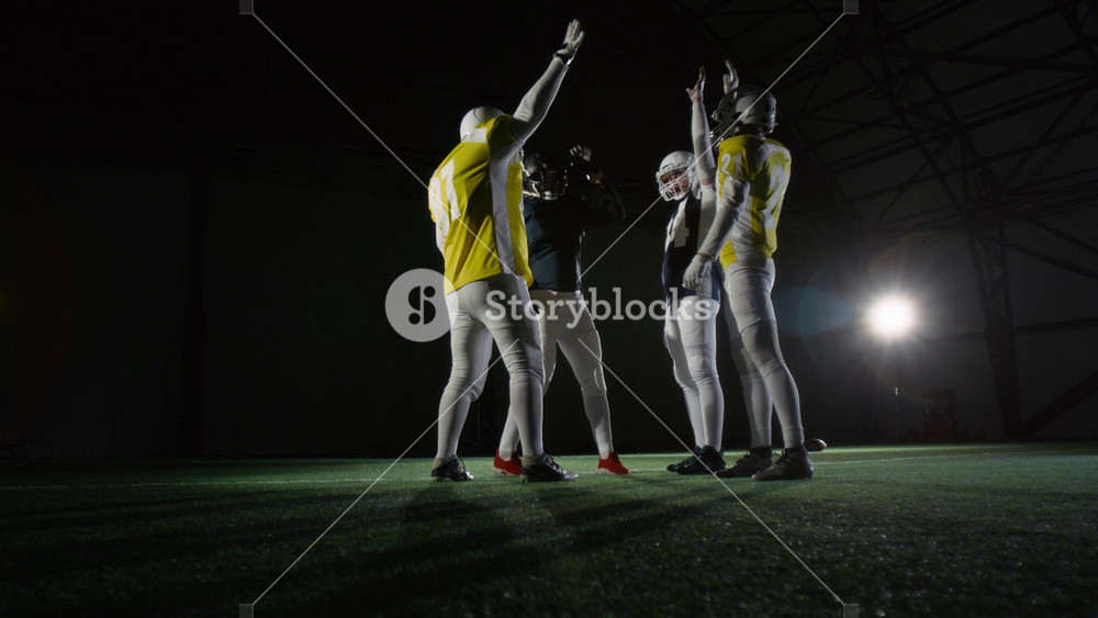 Wide shot of four male American football players joining hands in middle, then cheering and running off towards arena for training session, while preparing for match with rival team at amateur club