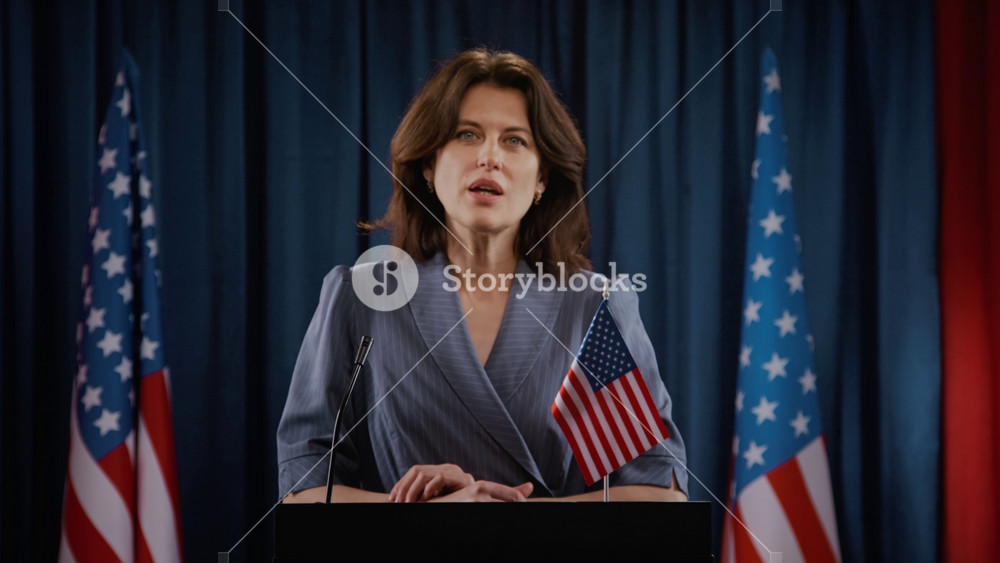 Portrait of adult woman politician speaking at podium with American flags in background. Clip is perfect for political campaigns, news broadcasts, or government public relations