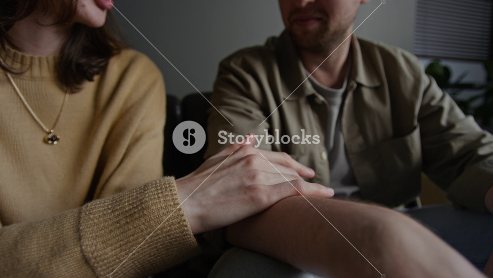 Close up shot of female hand following curve of male arm and holding hands while couple sitting on couch in therapy session, copy space