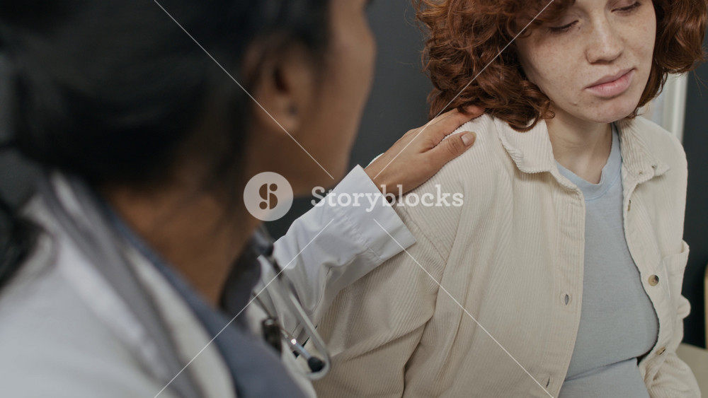 Hispanic female doctor comforting Caucasian pregnant young woman in clinic, placing hand on shoulder. Ideal for maternal healthcare and prenatal support campaigns