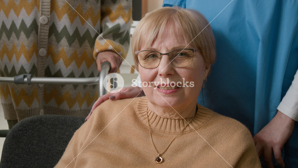 Portrait of senior woman smiling at camera in nursing home with caregiver standing nearby. Video for promoting geriatric healthcare and assisted living services