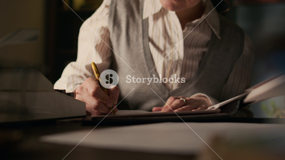 Tilt up shot of concentrated middle-aged Caucasian female writer wearing retro eyeglasses editing manuscript using fountain pen working on new chapter in her vintage study room