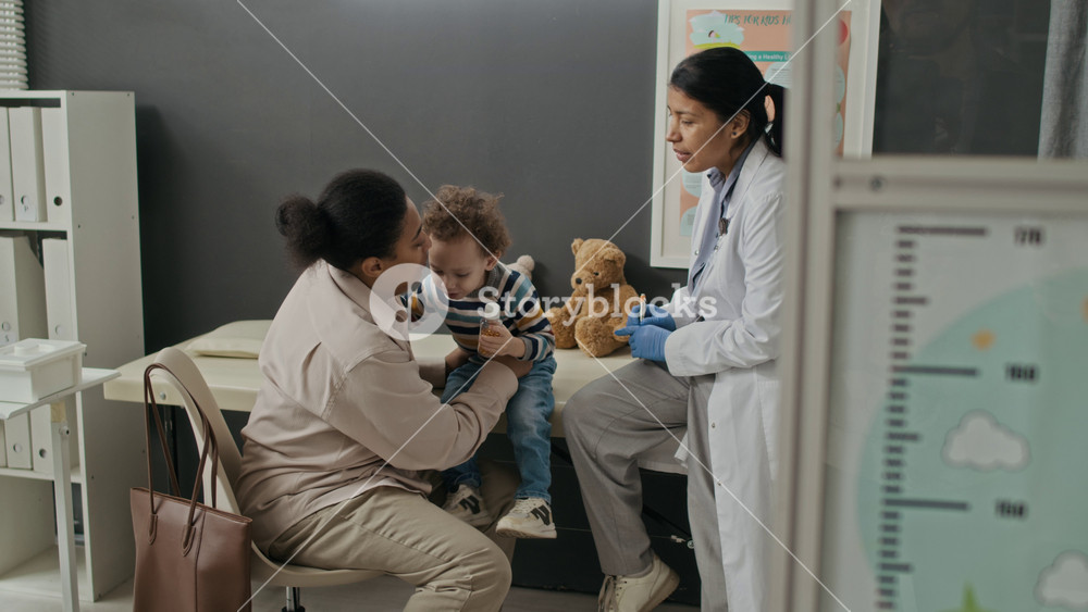 Biracial mother comforting toddler child during medical checkup with Hispanic female pediatrician in clinic. Perfect for pediatric healthcare services and family medicine marketing