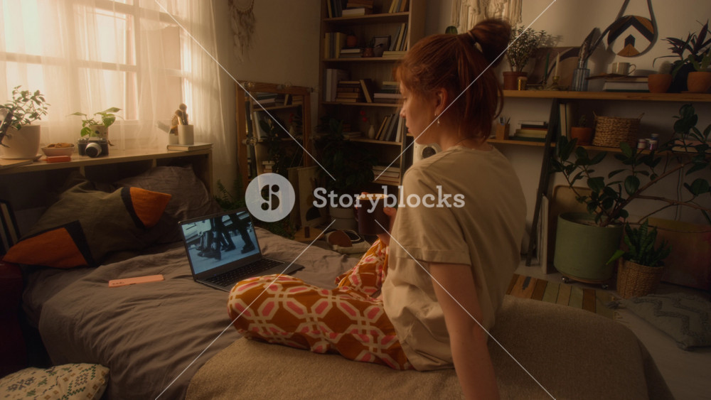 Full length shot of young woman watching videos or movies online with police troops on screen while sitting on bed at home and enjoying slow morning alone, copy space