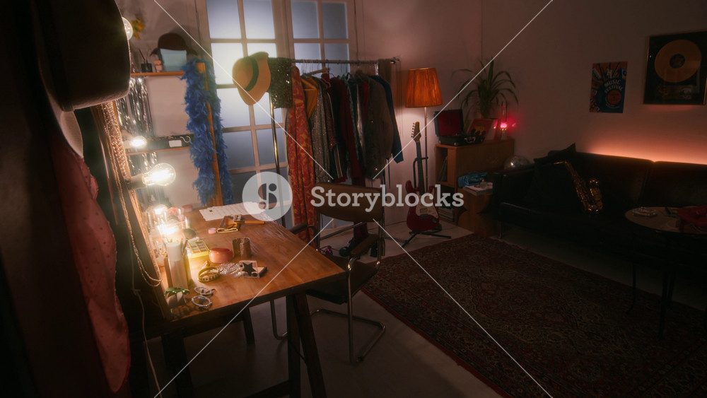 No people shot of interior of cozy little dressing room with warm, subdued lighting, dressing table, floor hanger with pile of clothes, electric guitar next to it, and sofa with tuba on it
