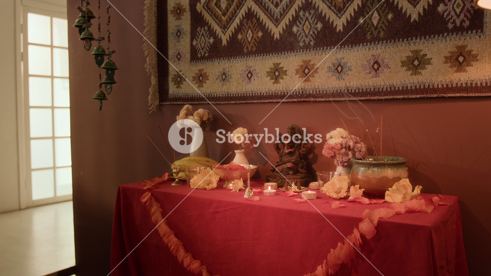 No people full shot of traditional home Hindu altar with statue of deity Ganesha, flowers, traditional decor placed on red tablecloth, warm light, copy space
