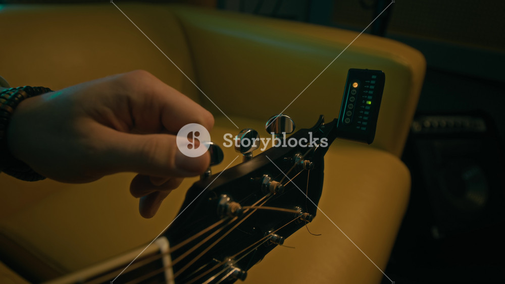 Close-up of hands of unrecognizable musician fixing digital electronic tuner clip on acoustic guitar headstock for tuning in neon lit room
