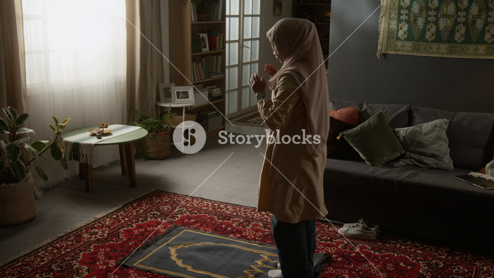 Wide angle shot of young Muslim woman wearing modest clothing staring daily prayer ritual and laying out prayer mat at home with traditional decor elements, copy space