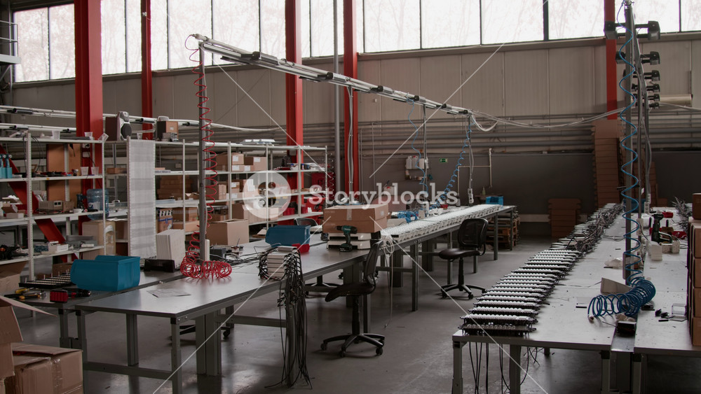 Wide no people shot of spacious workshop of industrial lighting factory, worktops with LED lamp components and tools for assembly, shelves with stock parts, chairs, in natural light in daytime