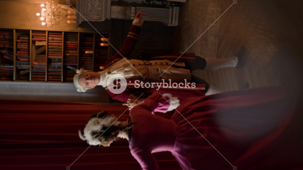 Vertical shot of young Caucasian noble lord in frock coat and breeches and lady in Victorian style dress performing courteous menuet dance during party or ball in palace hall
