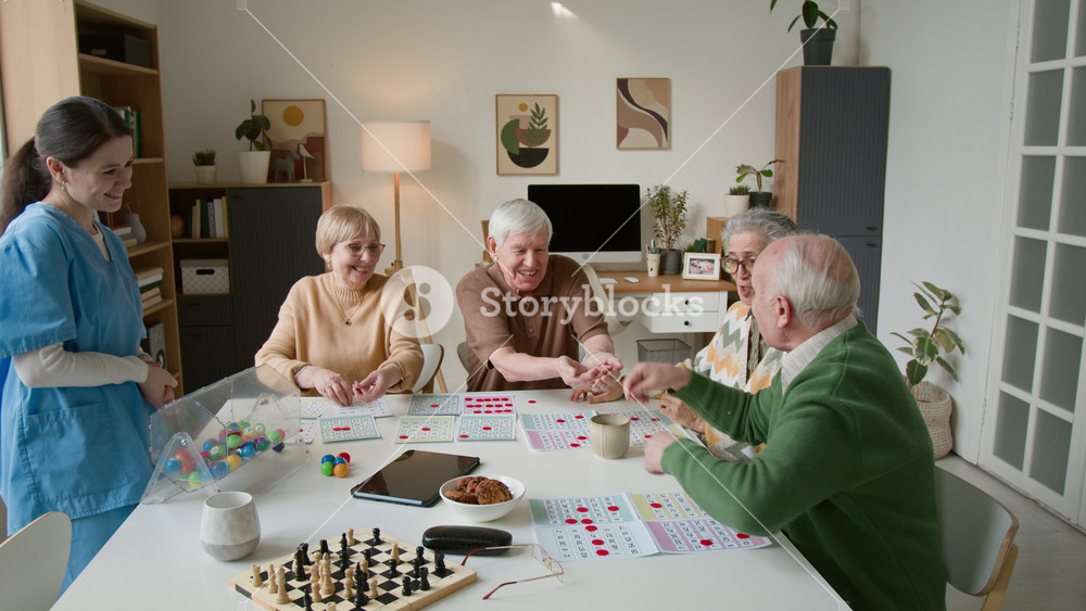Zoom in shot of seniors playing bingo with young female caregiver in retirement home, celebrating win. Footage promoting senior care facilities and active aging