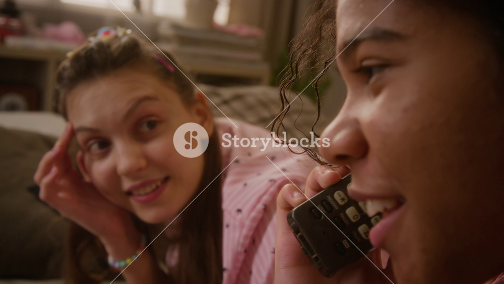 Close-up of African American teenage girl talking on retro cordless phone and laughing during sleepover with Caucasian teenage girl. Retro tech, youth friendship, and lifestyle advertisements