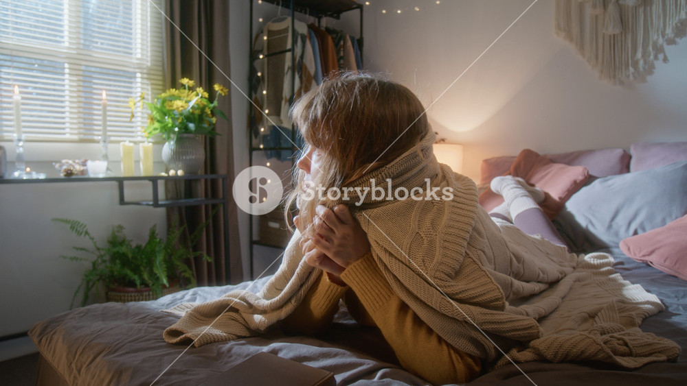 Young Caucasian woman reading book on bed, reacting to flashing lights by wrapping herself in blanket. Clip is ideal for home security, power outage services, or mental health campaigns