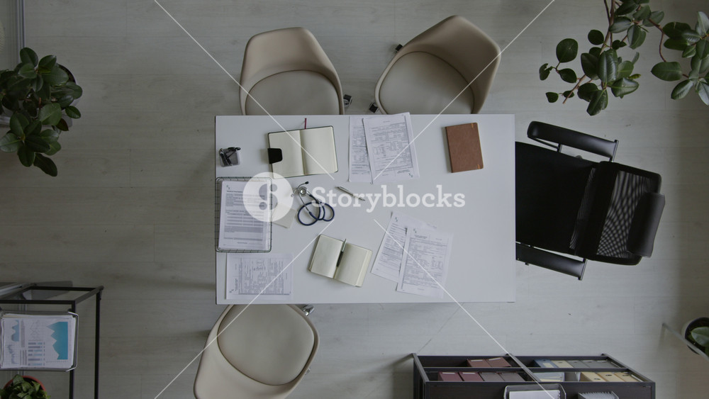 No people wide top view of desk in medical clinic office, with patient case files, clinical recommendations, stethoscope, doctors notebooks, several chairs, before staff meeting