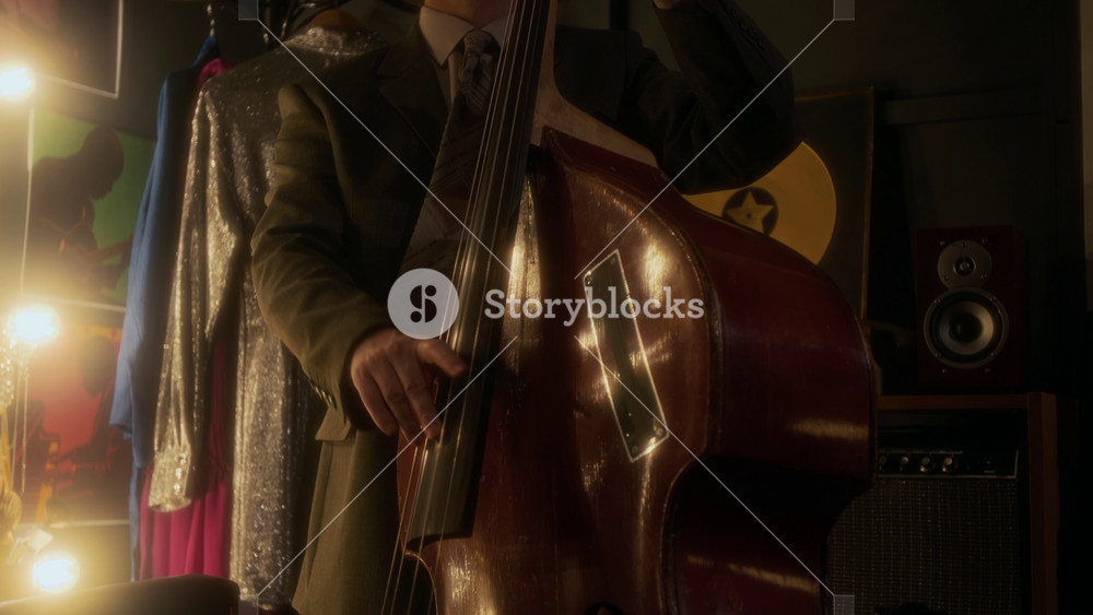 Low angle shot of adult Caucasian man wearing suit and hat playing upright bass backstage in jazz club