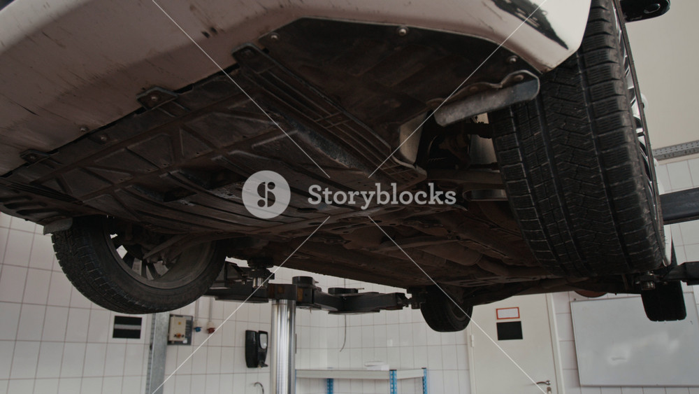 Below view of undercarriage and chassis of car mounted on heavy-duty hydraulic lift during suspension inspection to determine damage and breakdowns for overhaul and repair at auto garage