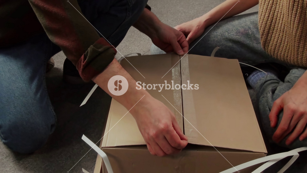 Medium zoom handheld shot of smiling middle-aged Caucasian couple revealing contents of flatpack package with DIY assembly cabinet, examining instruction, filmed by family member on digital camcorder