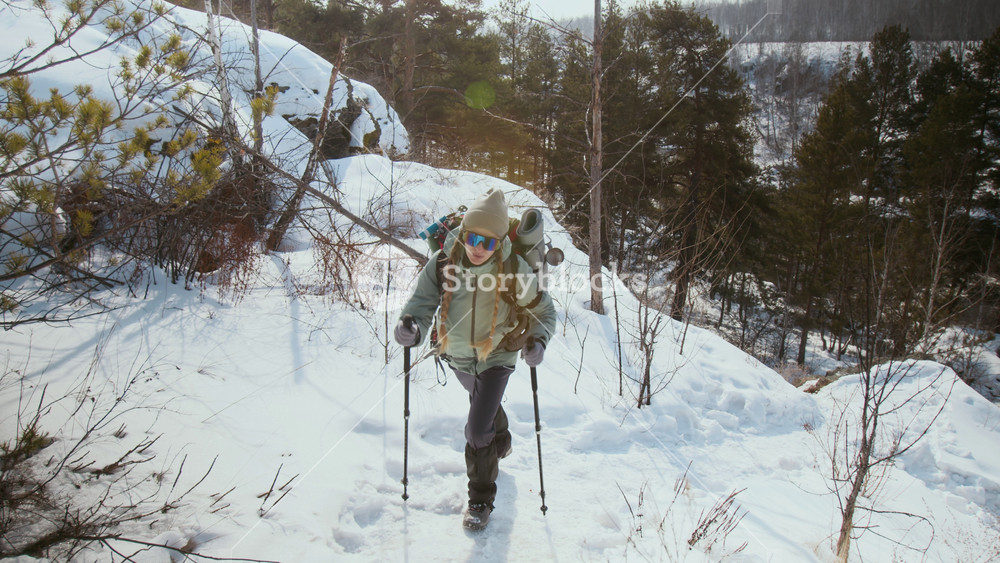 Cinematic shot of young woman enjoying beautiful winter hike in mountains and walking uphill with hiking poles, copy space