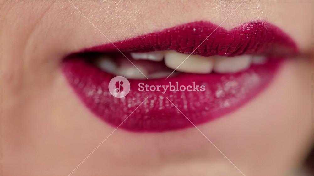 A close-up of a stunning woman’s lips as a make-up artist skillfully applies a deep, bloody lipstick, showcasing the artistry of beauty