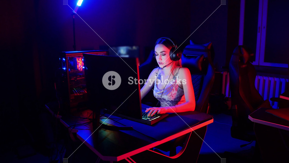 Gaming concept - young attractive woman with tattoos sits in the chair in neon gaming club and playing an online game