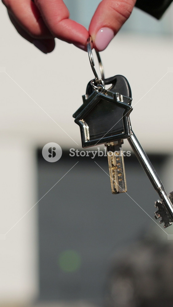 Vertical video Close-up of house key in the hand of woman house against the background. Real estate concept for buying a new home.
