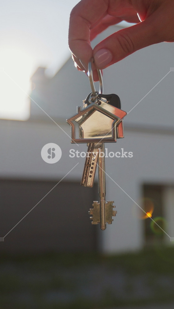 Vertical video Close-up of house key in the hand of woman house against the background. Real estate concept for buying a new home.