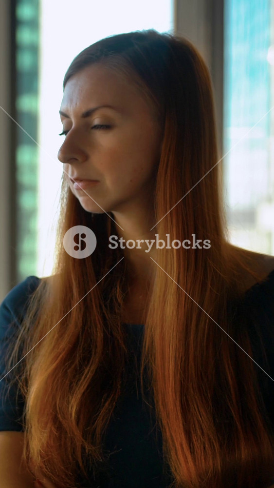 Vertical of Portrait of young successful redhair woman entrepreneur standing in office. Huge windows and business district background. | High Quality Visual