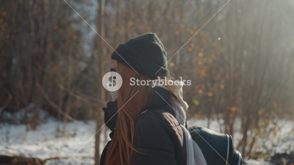 Woman walking outdoors. Snowy trail with backpack woman. Silhouetted woman on winter trail with hat. Rural winter scene showing woman with
