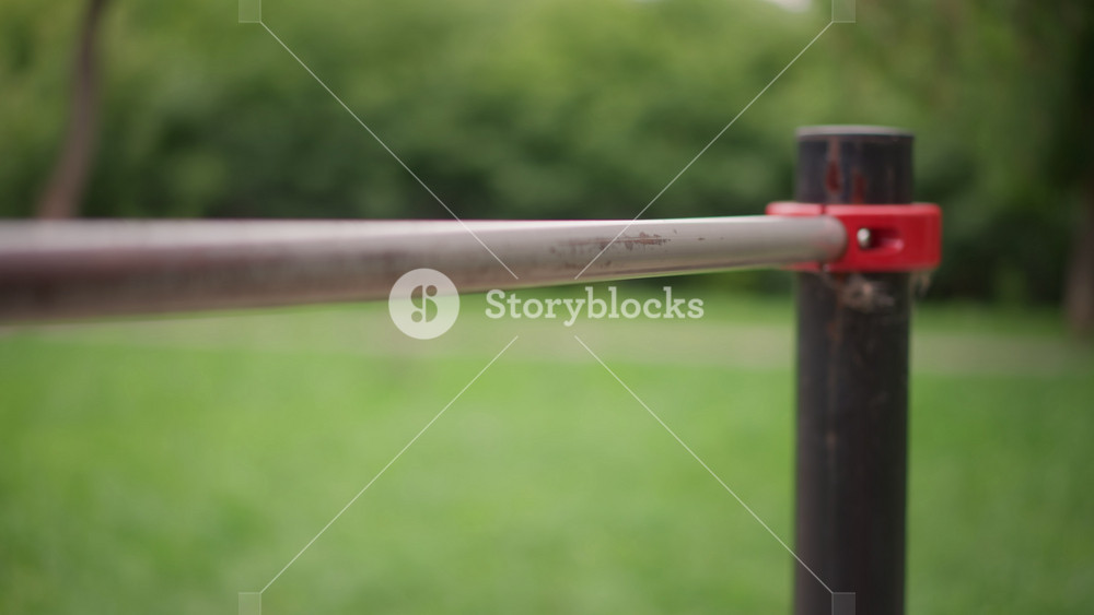 Person Securing Band On Metal Bar, Closeup Of Hands Tightening Resistance Band Onto Metal Bar At Park, Detailed Shot Of Person Securing Red