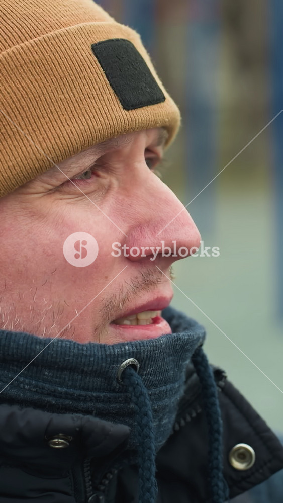 Close-up of a coach sitting on a workout equipment, looking tired as he gazes at the boys playing football in the blurred background