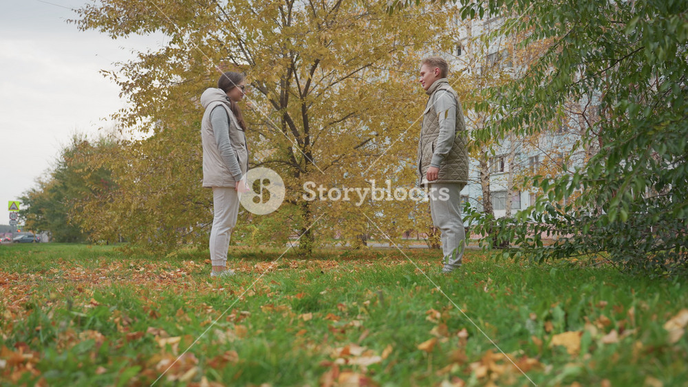 Young adult prepares to kneel and propose to fiancee in outdoor park as he reacts with surprise, surrounded by autumn leaves and trees with