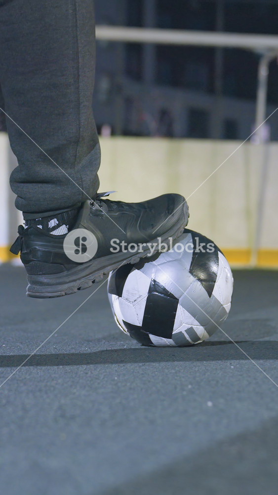 Close up back view of soccer player resting one foot on soccer ball on an outdoor sports field, wearing athletic shoes and sweatpants