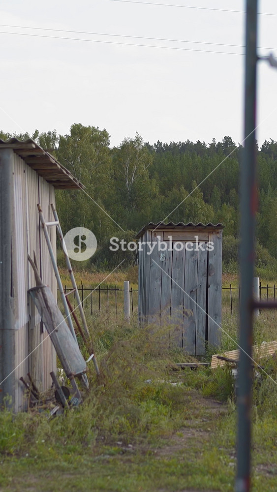 Barn with open door boards pile and outdoor handmade toilet in summerhouse yard. Small houses and construction materials in village