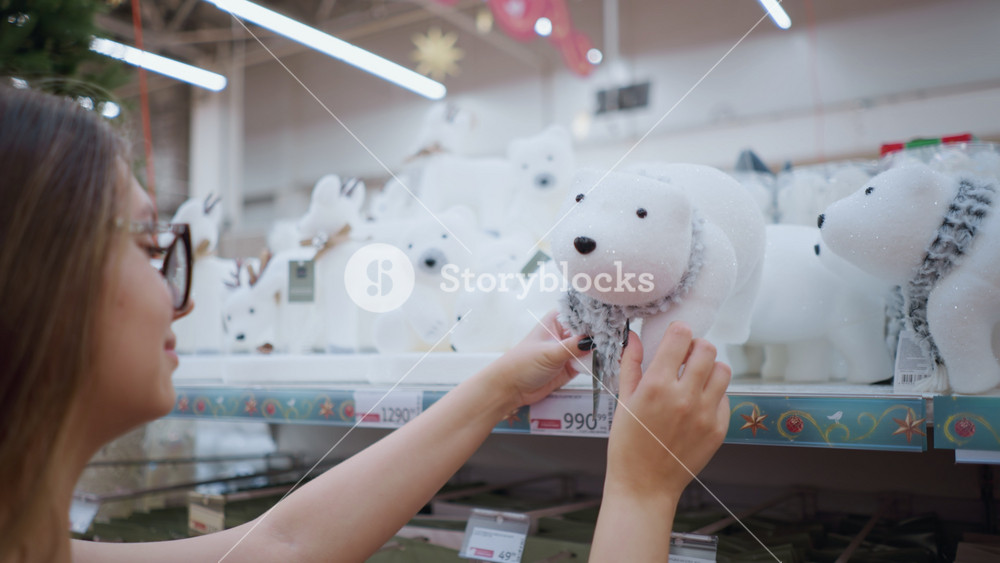 Side view of smiling woman with long brown hair wearing black shirt and adjusting white plush polar bear toy with scarf on store shelf
