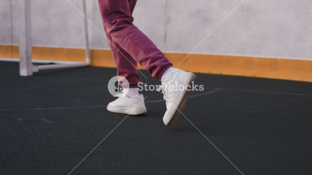 Leg view of female athlete jogging around curved barbed wire sports court under soft dusk sky, white sneakers stepping on smooth asphalt
