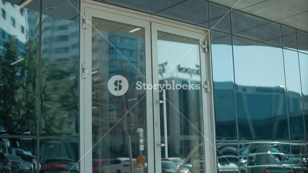 Back view of lecturer walking toward lecture building entrance with door handle reflecting busy urban street, cars, and modern cityscape