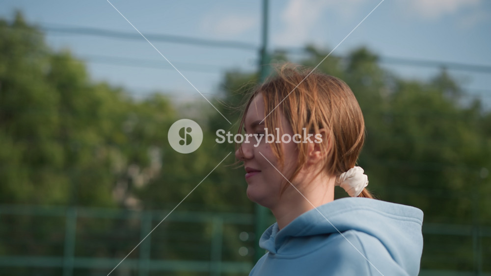 Close up of lady jogging as wind blows her hair across her face, wearing a blue hoodie, background features blurred view of people and