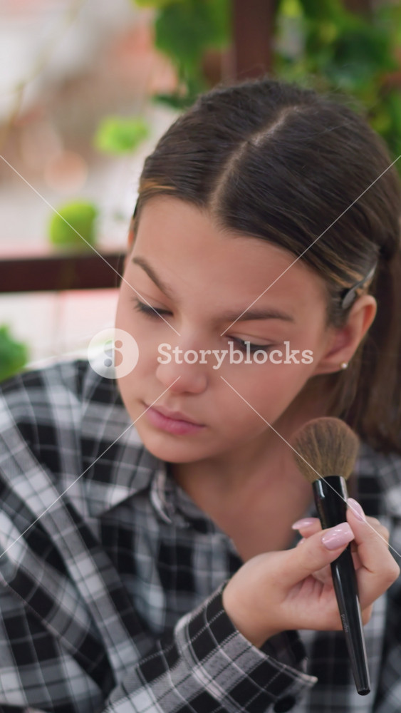 Youthful glow achieved, Teen girl gently powders face, White teenager softly blends bronzer on balcony, Teenage girl in plaid shirt uses