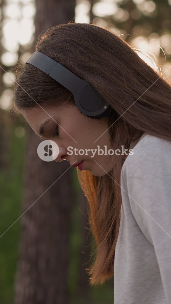 Sad lady with headphones in forest. Young woman looks upset listening to music thinking about loneliness during walk at sunset. Reflections