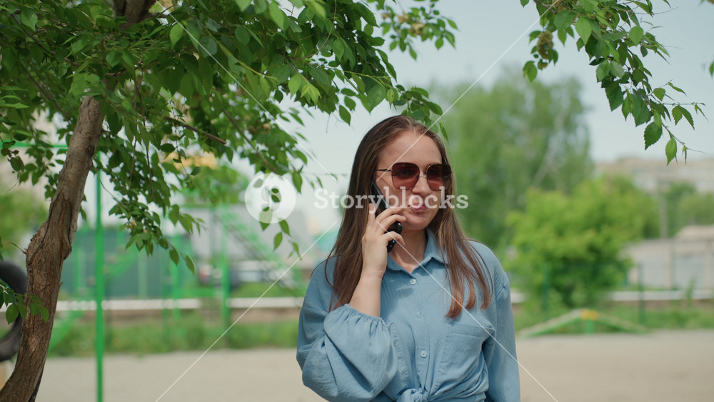 pensive lady talking under trees, relaxed woman in denim converse on call near playground swing, contemplative female in casual wear