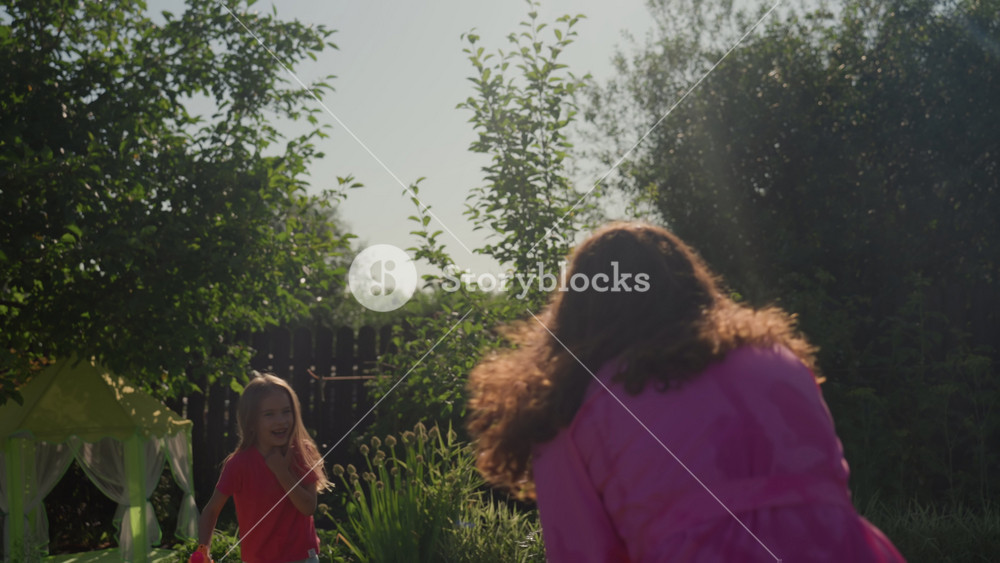 Child Enjoys Colorful Water Spray, Joyful Backyard Scene With Woman And Child Splashing Water, Happy Family Outdoor Activity Featuring Woman
