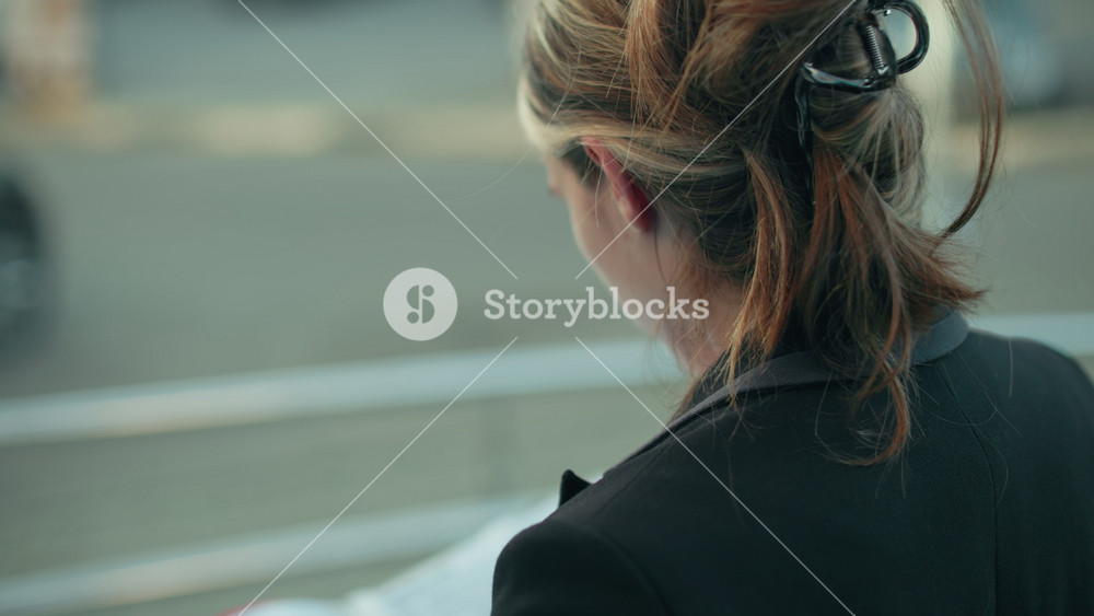 Close up rear view of woman in black suit reading file while standing beside metal railing with blurred view of parked cars and road
