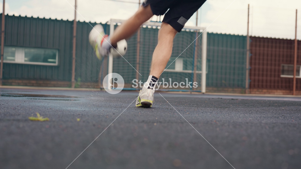 urban wet court soccer player white dribbles and kicks ball across rainslick asphalt near fence and basketball hoop, wearing jacket and