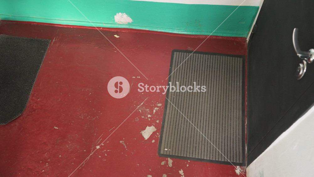 white courier lifts insulated food bag at apartment entrance. Red painted floor and green trim frame worn mat. Courier opens insulated bag