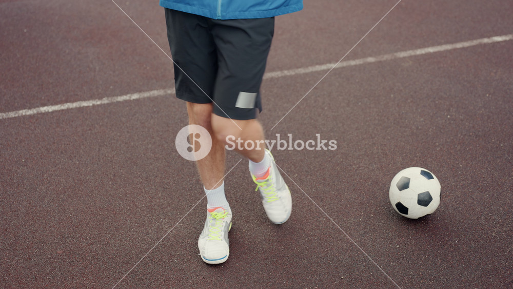 street court football player feet closeup steady touches on wet asphalt, neon sneakers tapping classic black white ball, focused warmup