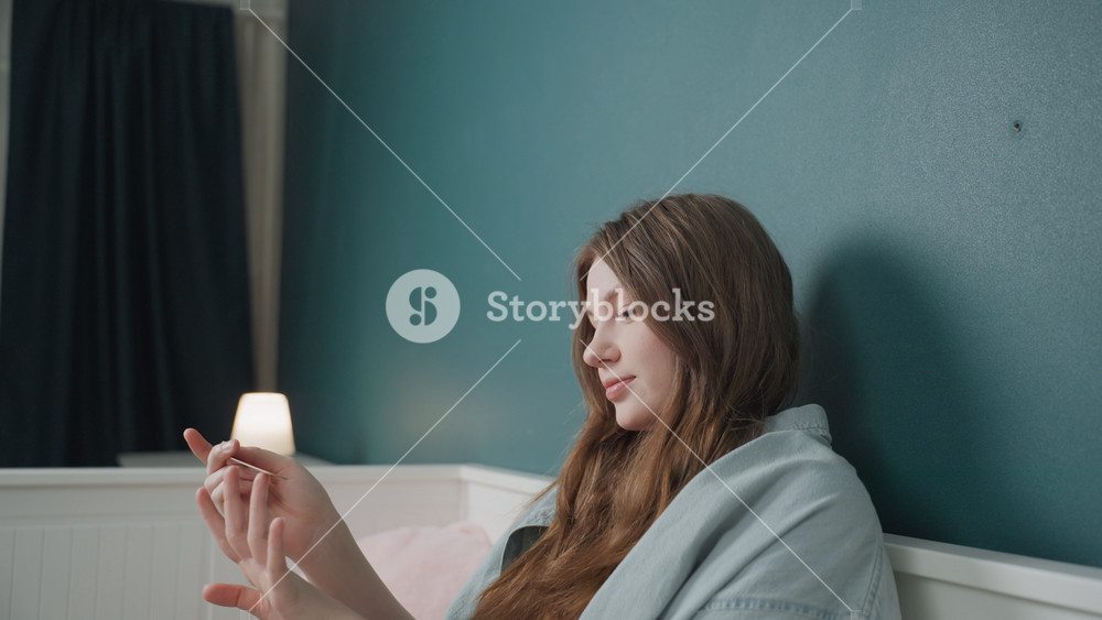 Caucasian teen laughing while filing nails, wrapped in blanket beside soft lamp, candid smile, cozy bedroom vibe, youthful downtime and